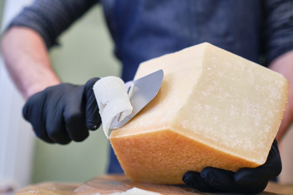 A male staff slicing a block of cheese in a local supermarket